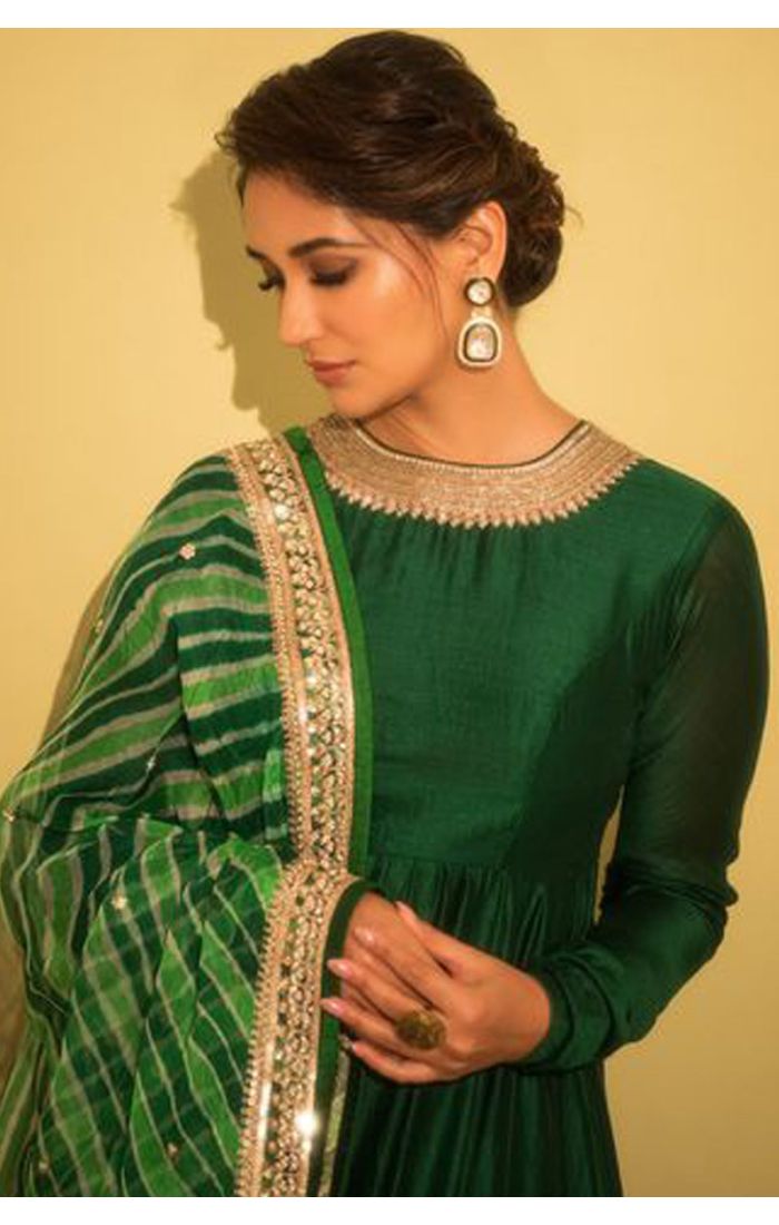 A model wearing a rich green Anarkali suit with a flowing silhouette, featuring full-length fitted sleeves and a satin-like finish. The outfit is paired with a green tie-dye patterned dupatta adorned with an embroidered border. Perfect for traditional cer